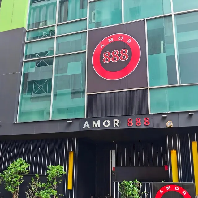 The entrance of Amor 888 on Sukhumvit Soi 18 by day: the round red 888 sign above the AMOR 888 fascia, a red step and potted trees
