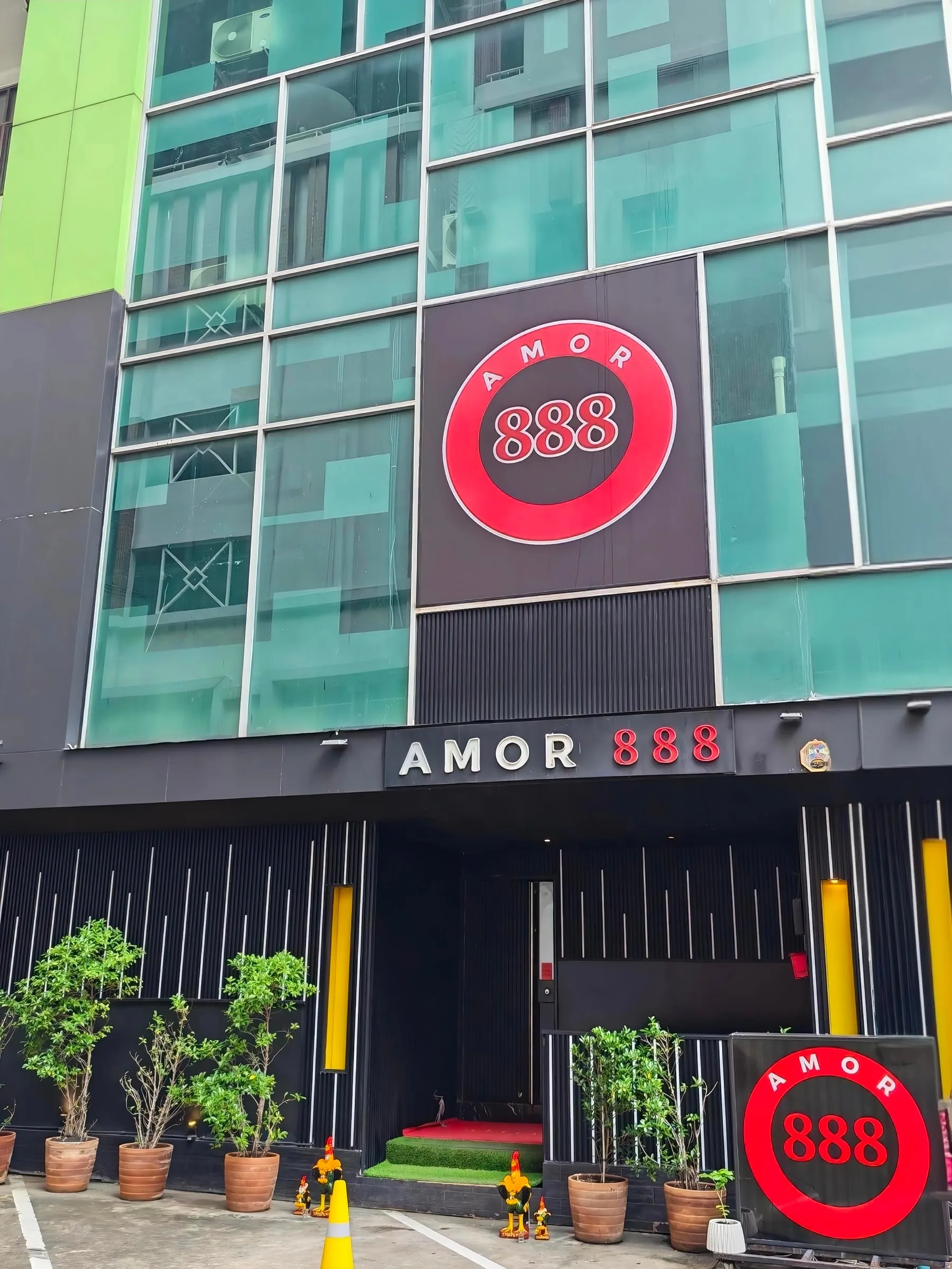 昼間のAmor 888の入口（スクンビット ソイ18）。AMOR 888の看板の上に赤い丸い888のロゴ、赤い段差と鉢植え