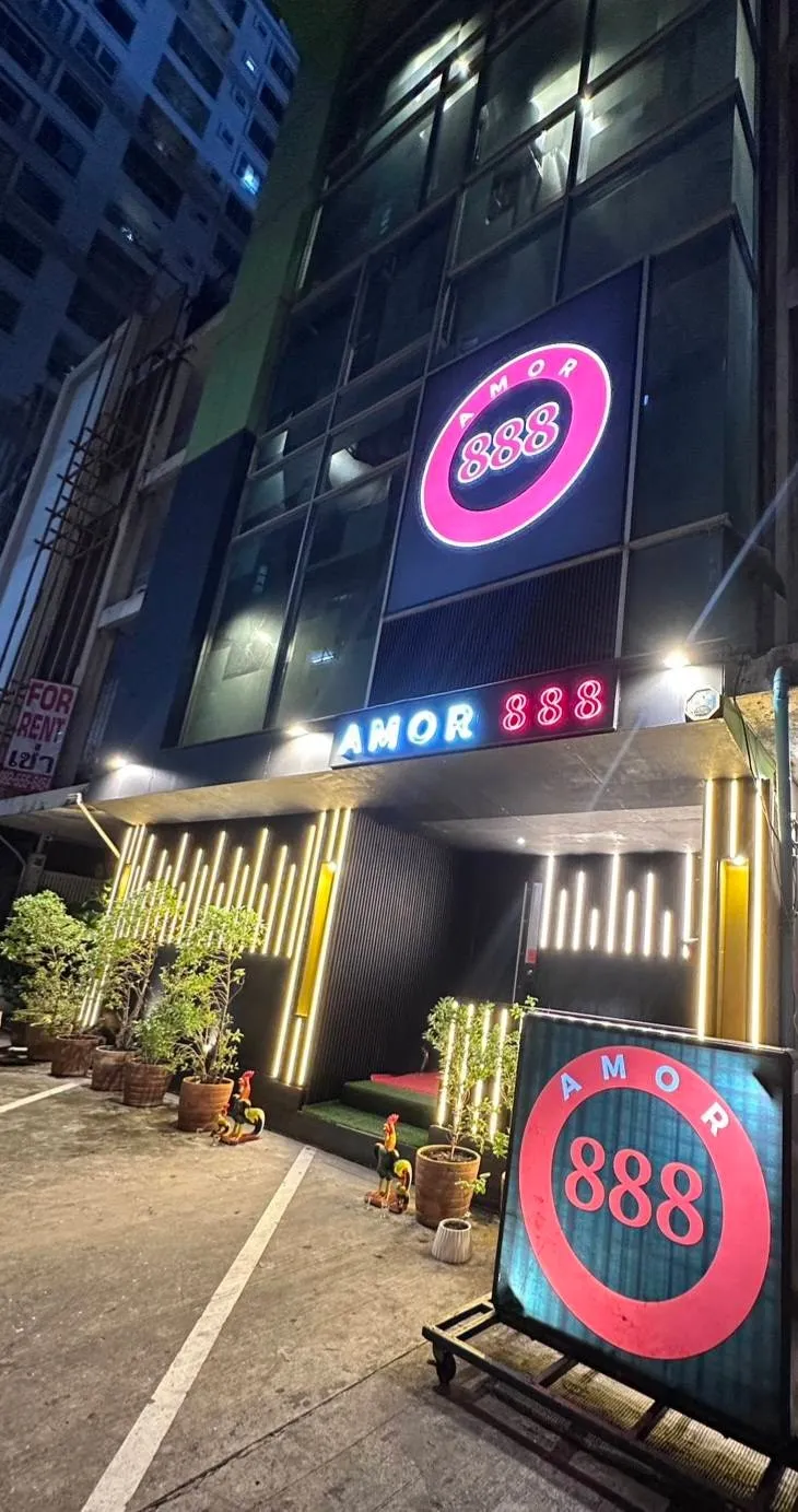 Amor 888 at night: the lit red 888 ring and the AMOR 888 sign over the entrance, light strips on the pillars and potted trees in front